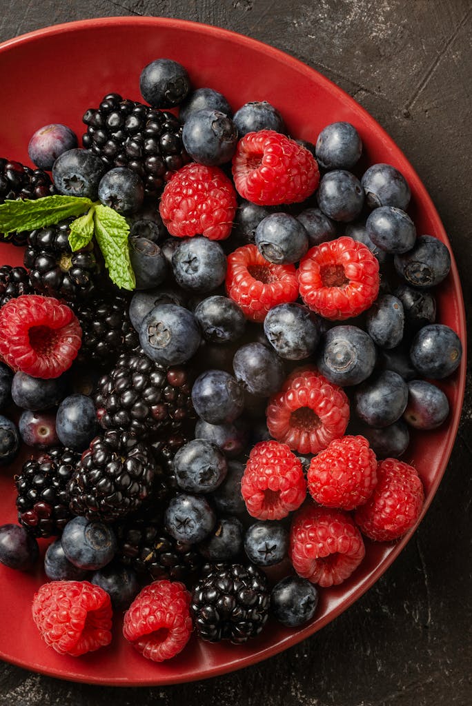 Fresh blackberries, blueberries, and raspberries on a red plate from above.